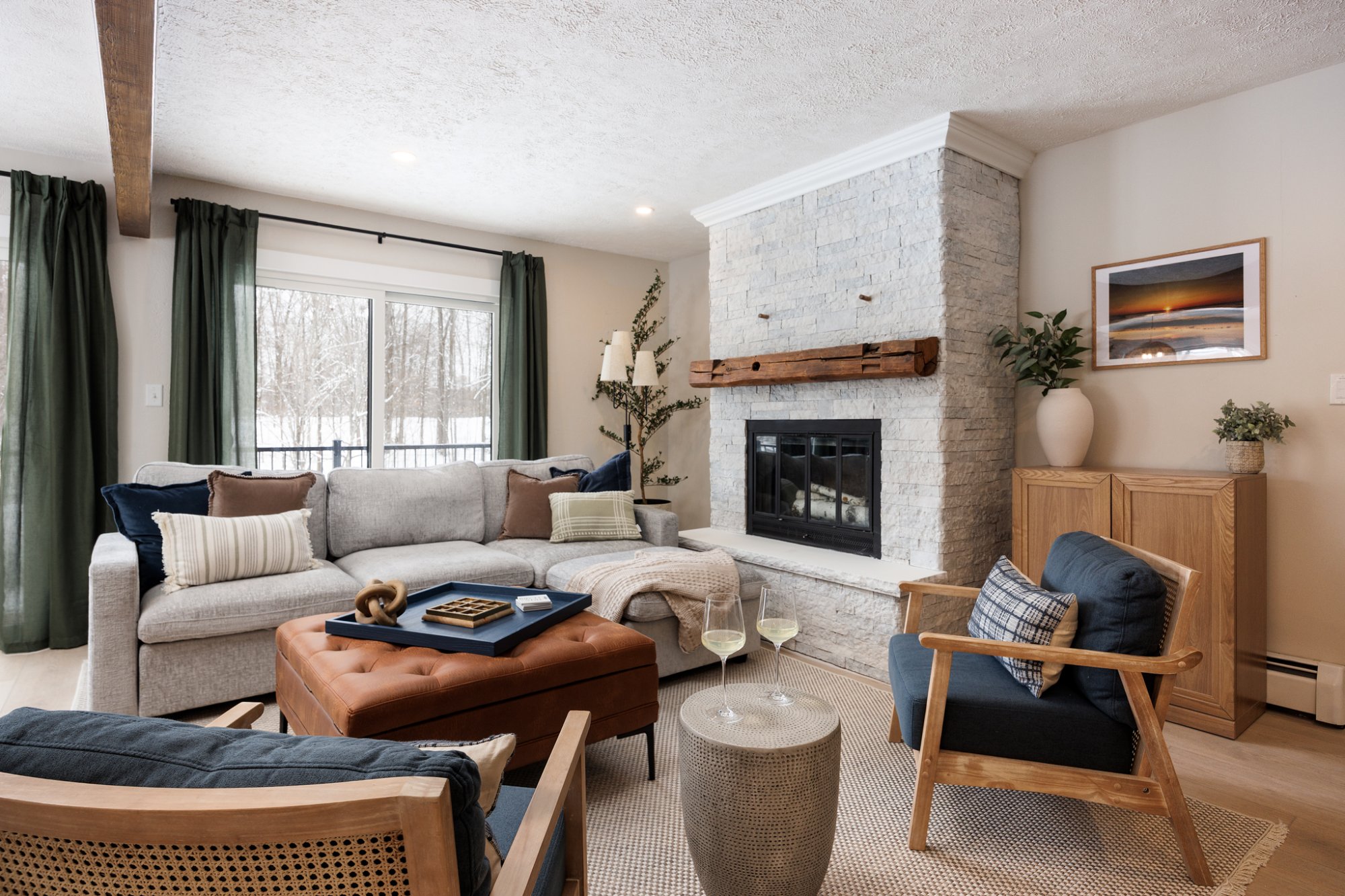 Birch + Still living room with stone fireplace, sectional sofa, and green curtains